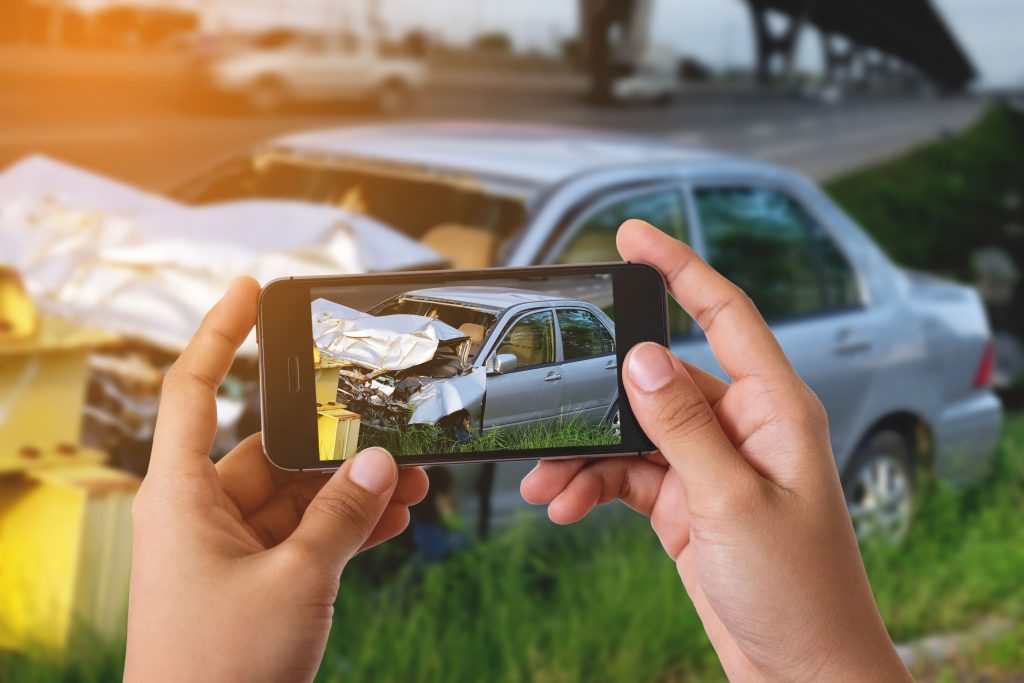 Hand holding a phone taking a picture of a damaged car
