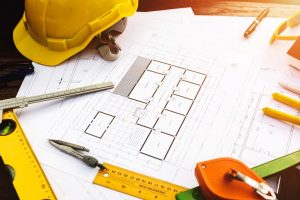 Floor plan drawing with contractor related items spread around like rulers, glasses, pens, measuring tape and a hard hat